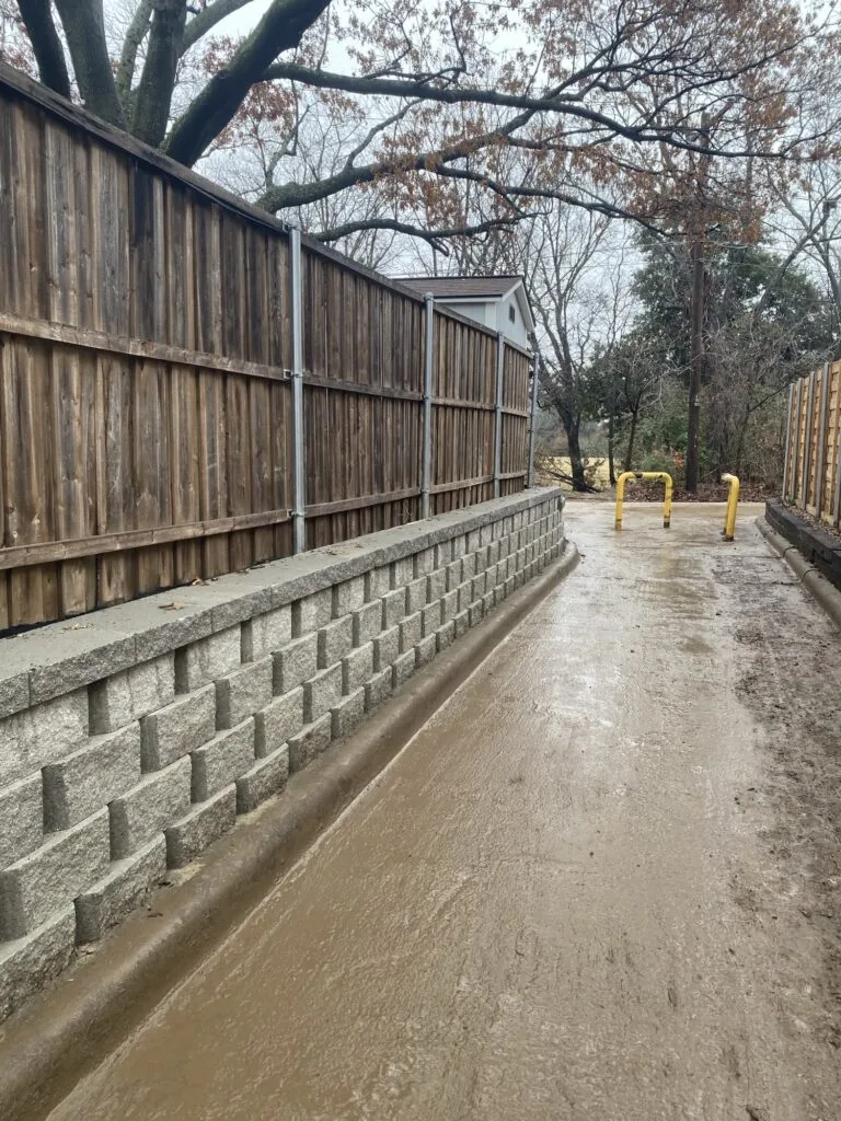 New concrete block retaining wall supporting a wood fence along a narrow alley in Dallas, TX, replacing an old crosstie wall