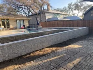 Multi-tier concrete block retaining wall with cap replacing old cross ties beside residential pool patio in Dallas TX