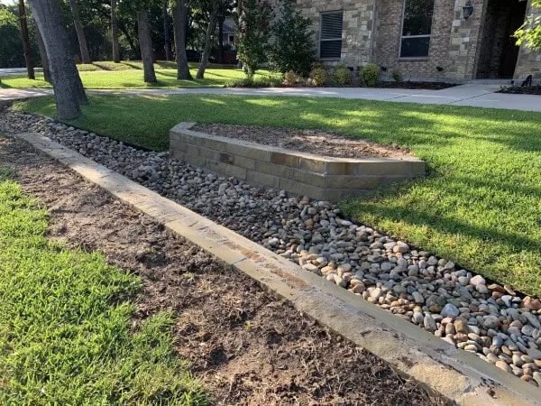 Concrete block retaining wall with river rock drainage channel along residential front yard in Southlake TX