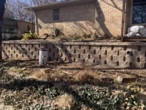 Aging concrete block retaining wall with weep holes along residential backyard in Arlington TX, awaiting replacement
