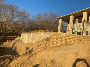 New concrete block retaining wall replacing failed railroad-tie wall beside residential home in Carrollton TX, freshly backfilled with graded soil