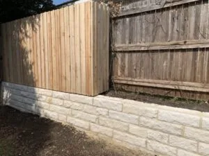 New concrete block retaining wall replacing a failing wood fence base along a residential backyard in Fort Worth TX
