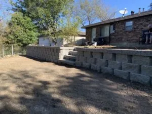 New concrete block retaining wall with built-in steps replacing old timber wall beside brick home in Fort Worth TX
