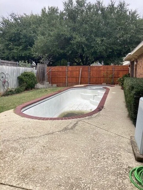 Drained residential inground pool with brick coping and concrete surround before pool removal in Flower Mound TX