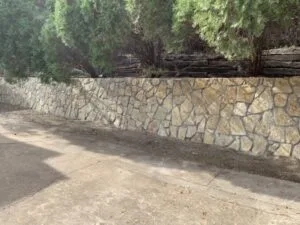 New Granbury stone retaining wall replacing a failing railroad-tie wall along a concrete driveway in Fort Worth, TX