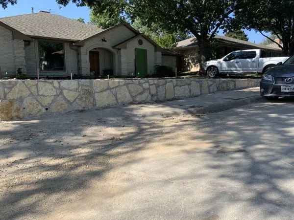 Granbury stone retaining wall along front yard of brick ranch home in Dallas, TX, creating level driveway edge