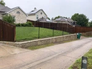 Completed Milsap stone retaining wall replacing old railroad cross ties along residential driveway in McKinney TX, topped with black iron fence