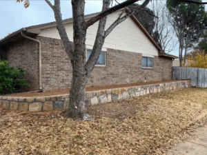 New Milsap stone retaining wall along brick home's foundation in Bedford TX, replacing old cross-tie wall with fresh backfill and raised planting bed