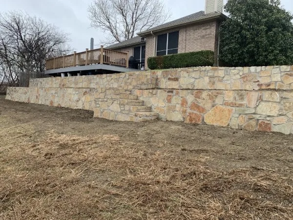 Large Milsap stone retaining wall with built-in steps supporting a wood deck behind a brick home in Carrollton TX