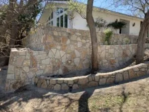Milsap stone retaining wall replacing old cross ties at a Carrollton TX home, with curved lower accent wall and white house visible above