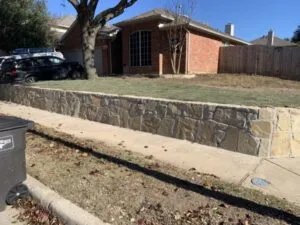 New Milsap stone retaining wall along residential front yard in Fort Worth TX, holding elevated lawn beside sidewalk