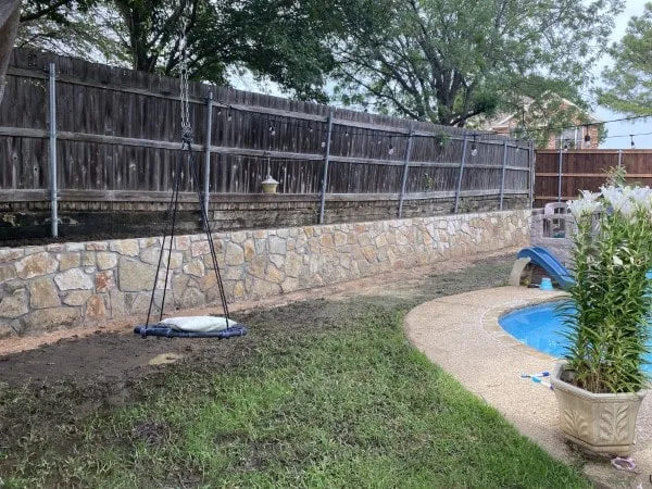 Completed Milsap stone retaining wall replacing old cross ties along wood fence line in backyard near pool, Euless TX