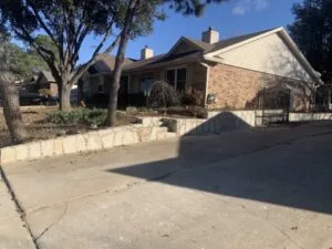 New Milsap stone retaining wall replacing old crosstie wall along front driveway of brick home in Euless TX