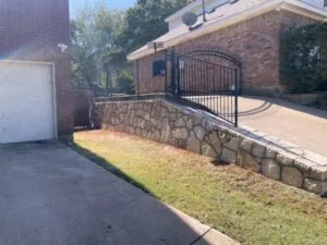 Milsap stone retaining wall replacing old railroad ties alongside driveway near iron gate at brick home in Euless TX