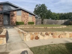 Milsap stone retaining wall lining front yard and walkway of brick home in Grand Prairie, TX, replacing a failing block wall