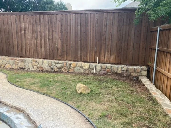 Milsap stone retaining wall running along a wood privacy fence in a Highland Village backyard, replacing a failed railroad-tie wall