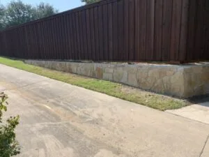 New Milsap stone retaining wall along driveway beneath wood privacy fence, replacing failing wall in McKinney TX