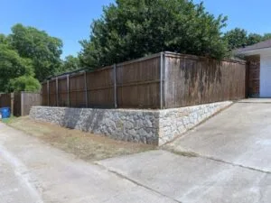 Milsap stone retaining wall replacing old cross-tie wall with wood privacy fence reinstalled on top, residential yard in Coppell TX
