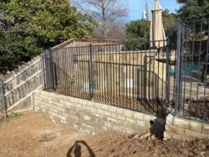 Completed Milsap stone retaining wall replacing old cross-tie wall, topped with wrought-iron fence beside backyard pool in Plano, TX