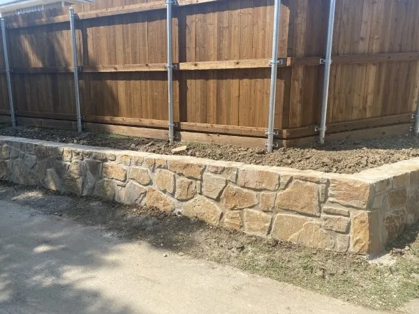 Newly built Milsap stone retaining wall replacing a railroad tie wall along a wood privacy fence in Garland, TX