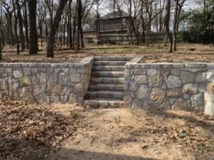 Milsap stone retaining wall with built-in center staircase replacing old wood wall on wooded Fort Worth-area residential property