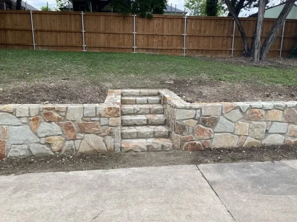 Newly built Milsap stone retaining wall with integrated stone steps leading from sidewalk to upper yard level in Dallas, TX