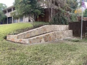 Newly built two-tier Milsap stone retaining wall replacing old cross-tie wall on sloped backyard in Fort Worth TX