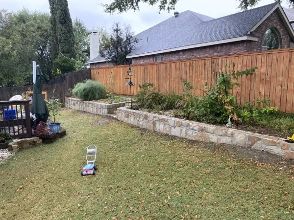 Completed Milsap stone retaining wall replacing old cross-tie wall in Carrollton TX backyard with raised planting bed