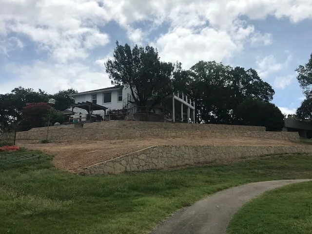Multi-tier natural stone retaining walls terracing a sloped residential yard in Fort Worth TX, with home and covered porch above