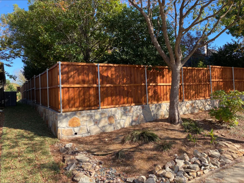 Natural stone retaining wall with drainage weep hole supporting a cedar fence along a sloped residential yard in Carrollton TX