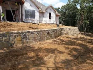 New natural stone retaining wall built along front of home under construction in Carrollton TX, DFW clay soil graded and exposed