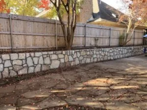 Natural stone retaining wall replacing old wood fence-base wall along backyard patio in Arlington, TX