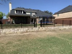 Natural stone retaining wall with black iron fence along residential backyard in Frisco TX, leveling sloped yard behind brick home