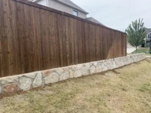 Low natural stone retaining wall supporting a wood privacy fence along a leveled residential yard in Hickory Creek TX