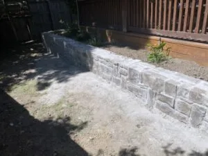 L-shaped concrete block retaining wall rebuilt in a residential backyard near wood privacy fence, Fort Worth TX