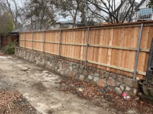 Natural stone retaining wall with cedar privacy fence on top, replacing failed crosstie wall along residential property in Carrollton TX