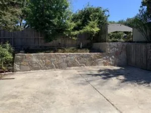 Granbury or Milsap stone retaining wall replacing old crosstie wall along concrete patio in Fort Worth TX backyard