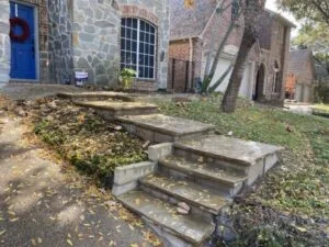 Aging stone retaining wall and concrete steps at a Dallas home's front entry, showing settlement and wear on a sloped yard