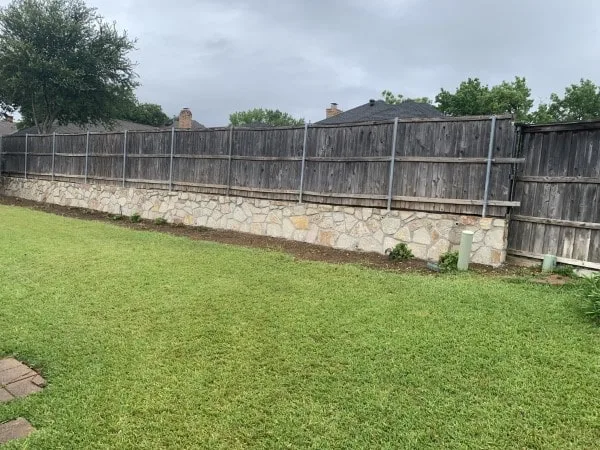 Natural stone retaining wall replacing old railroad-tie wall along wood privacy fence in Arlington TX backyard