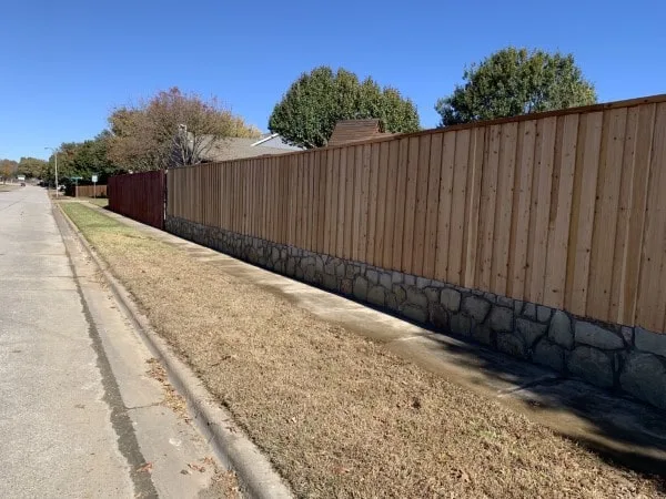 Stone retaining wall base supporting a wood privacy fence along a residential street in North Richland Hills, TX — crosstie wall replacement
