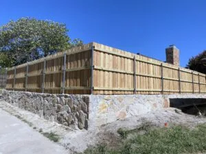 New Granbury stone retaining wall with wood privacy fence on steel posts replacing old crosstie wall in The Colony TX