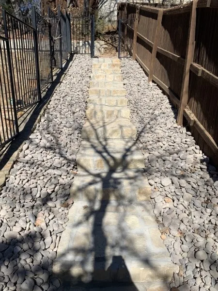 Granbury stone step pathway flanked by river rock gravel between wood fence and iron gate in Highland Village TX