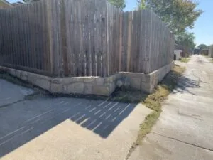 Low stone retaining wall replacing old wood crosstie structure along fence corner in The Colony TX residential alley