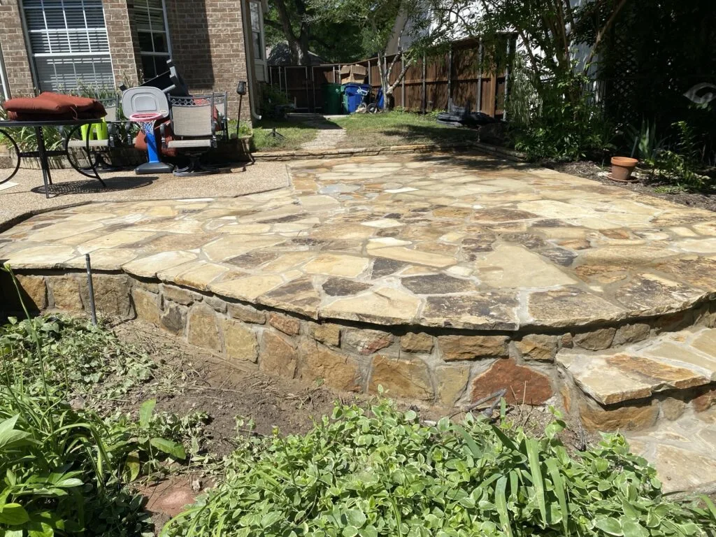 Curved Milsap stone retaining wall supporting a flagstone patio in a DFW backyard, replacing an old railroad-tie wall