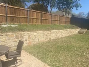 New Milsap stone retaining wall with integrated stone steps in a North Richland Hills backyard, replacing an old cross-tie wall