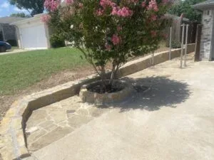 Natural stone retaining wall with circular tree ring planter and flagstone border along residential driveway in Fort Worth TX