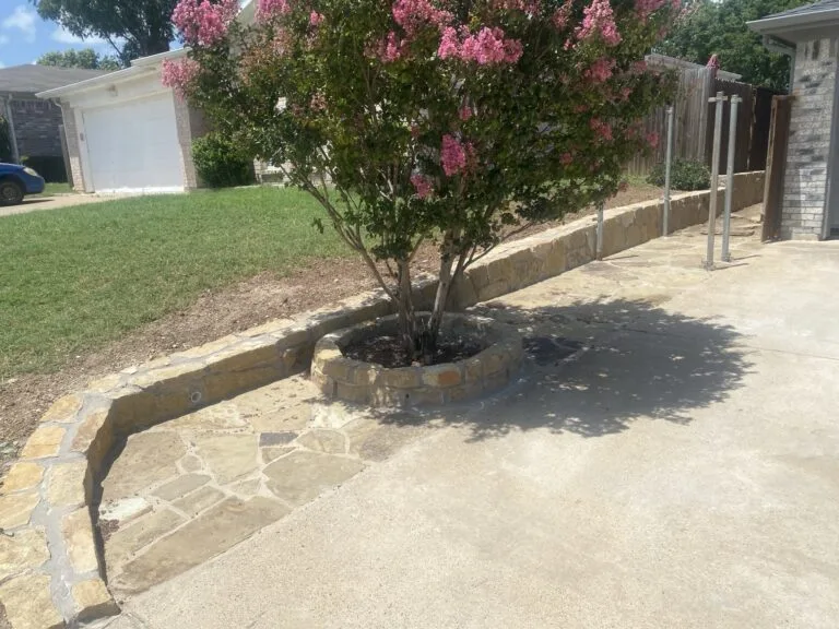 Natural stone retaining wall with circular tree ring planter and flagstone border along residential driveway in Fort Worth TX