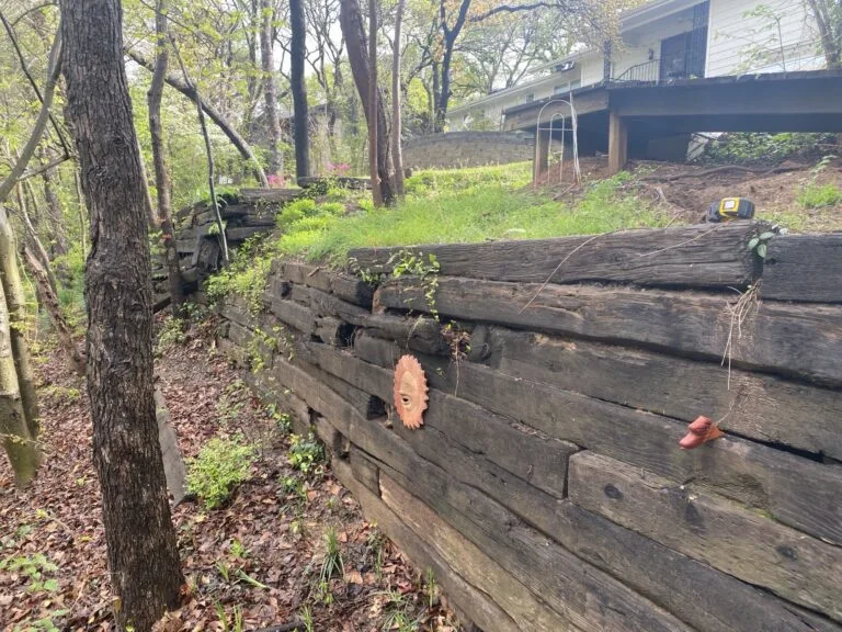 Aging railroad tie retaining wall bowing and deteriorating on a wooded residential slope in Bedford TX, before replacement