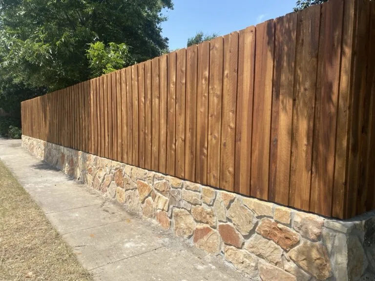 New Granbury stone retaining wall base supporting a cedar wood privacy fence along a sidewalk in Frisco TX