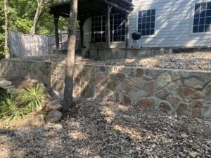 Milsap stone retaining wall replacing old crosstie wall behind a Fort Worth home, with gravel ground cover and covered patio above